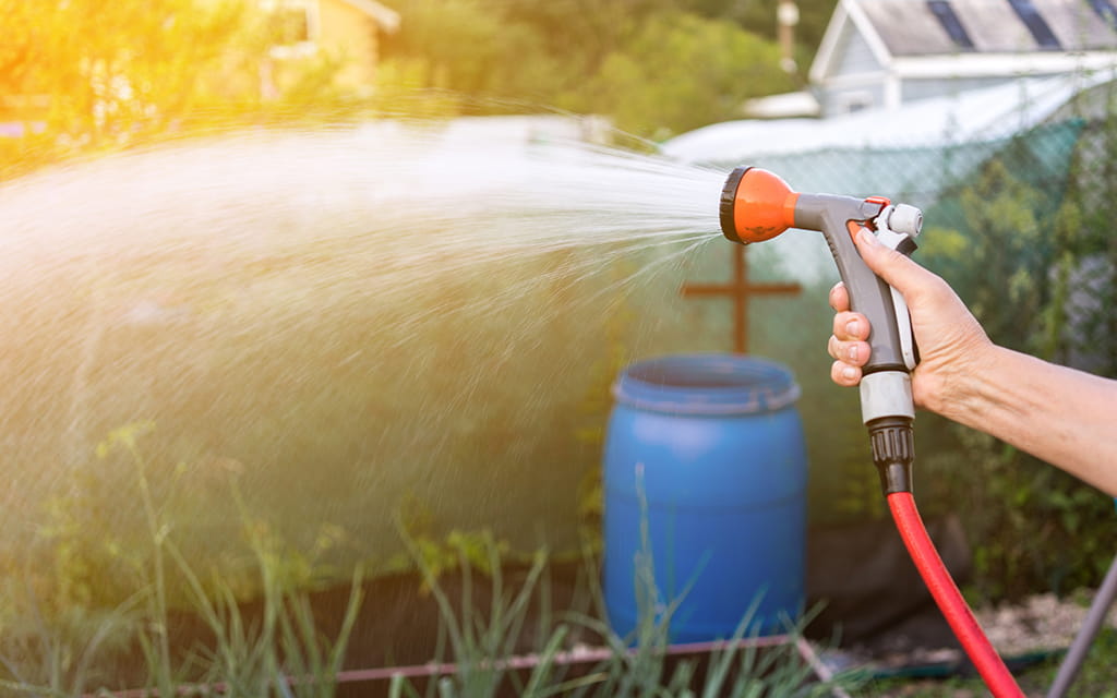 Wasser aus Gartenschlauch mit Regentonne im Hintergrund