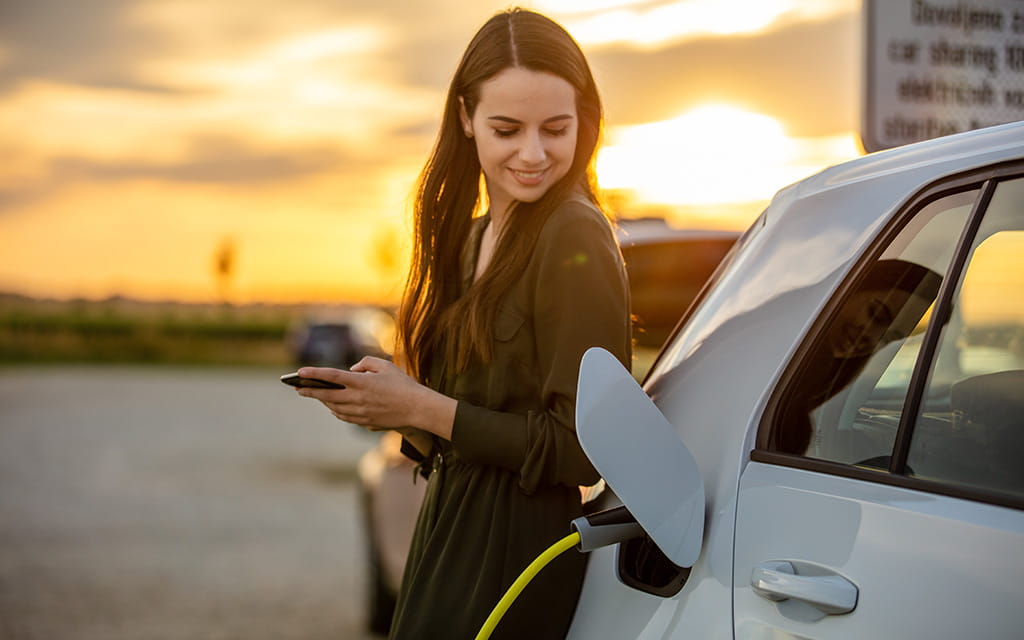 Frau steht neben einem ladenden Elektroauto