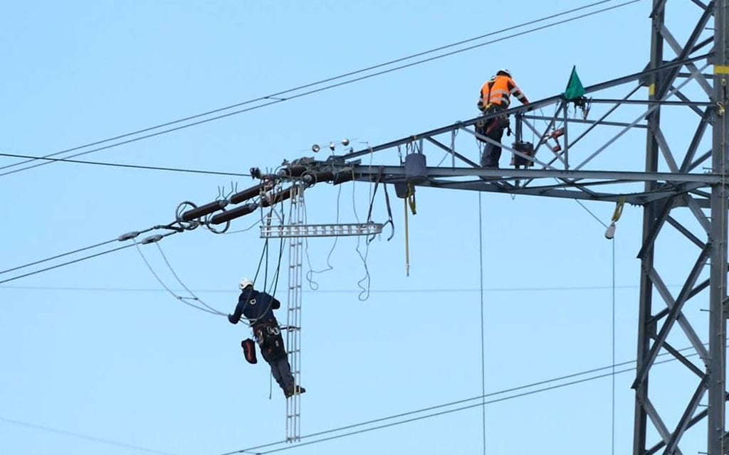 Zwei Männer auf einem Strommast, einer davon seilt sich gerade ab