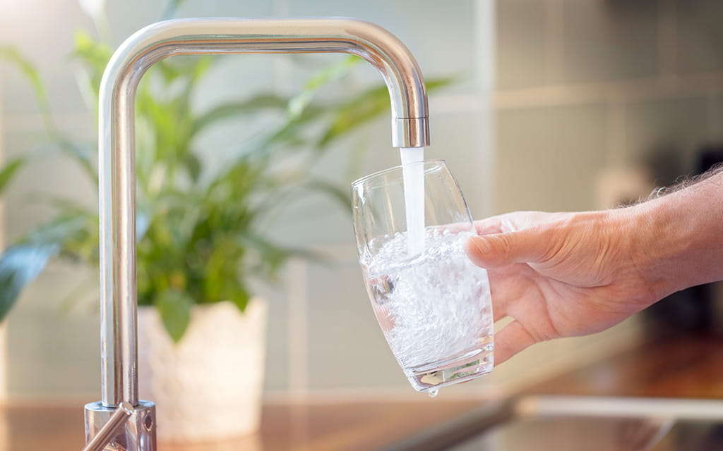 Person schenkt sich ein Glas aus dem Wasserhahn ein