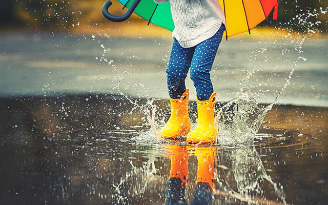 Kind springt in eine Regenpfütze