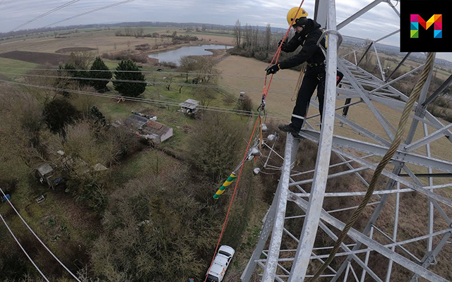 Ein Mann mit einem gelben Helm arbeitet auf einem Strommast