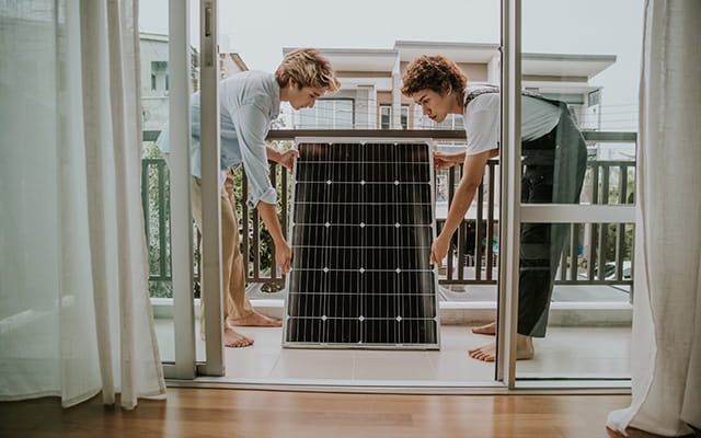 Zwei Frauen halten eine Solarplatte auf einem Balkon